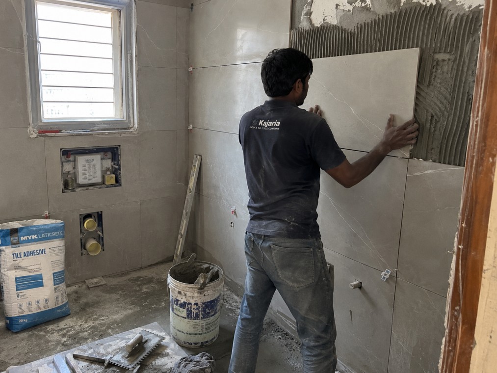 Wall tiles being fixed with tile adhesive in an Indian bathroom